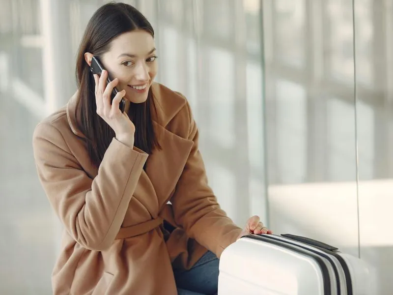 Passenger smiling with suitcase using mobile phone