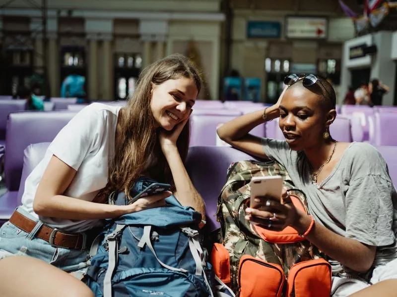 Two travelers sitting in terminal looking at phone